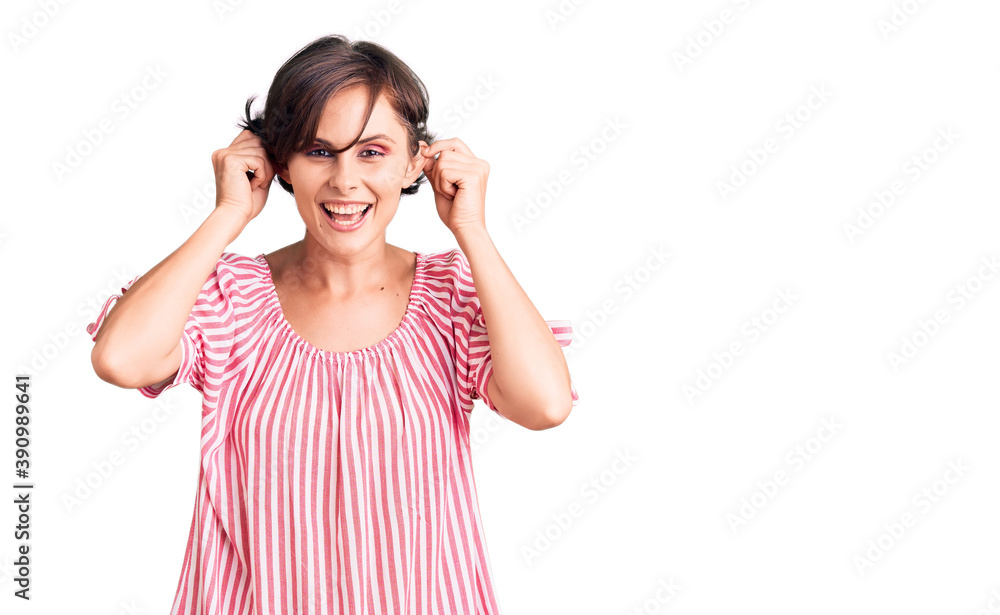 Beautiful young woman with short hair wearing casual summer clothes smiling pulling ears with fingers, funny gesture. audition problem Beautiful young woman with short hair wearing casual summer clothes smiling pulling ears with fingers, funny gesture. audition problem