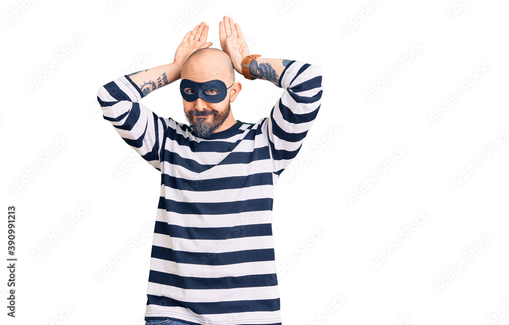 Young handsome man wearing burglar mask doing bunny ears gesture with hands palms looking cynical and skeptical. easter rabbit concept. Young handsome man wearing burglar mask doing bunny ears gesture with hands palms looking cynical and skeptical. easter rabbit concept.