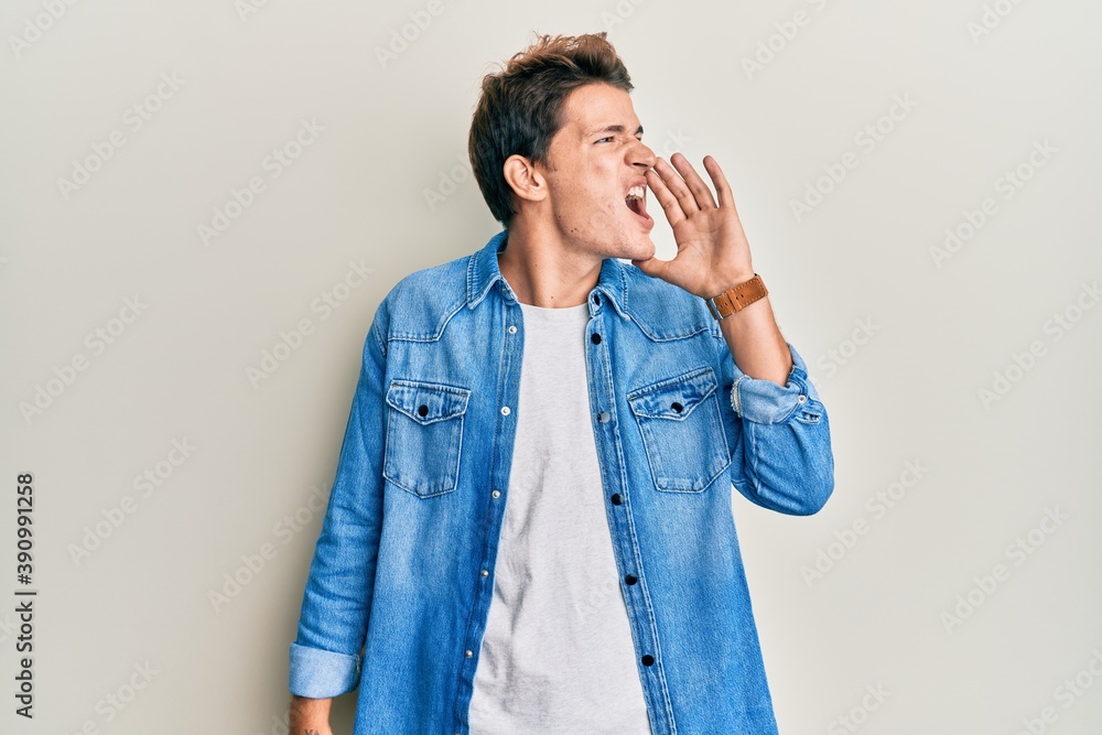 Handsome caucasian man wearing casual denim jacket shouting and screaming loud to side with hand on mouth. communication concept. Handsome caucasian man wearing casual denim jacket shouting and screaming loud to side with hand on mouth. communication concept.