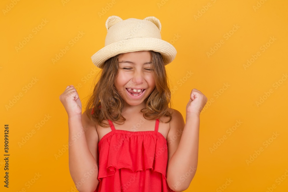 young Caucasian girl standing against yellow background rejoicing her success and victory clenching fists with joy being happy to achieve aim and goals. Positive emotions, feelings. young Caucasian girl standing against yellow background rejoicing her success and victory clenching fists with joy being happy to achieve aim and goals. Positive emotions, feelings.