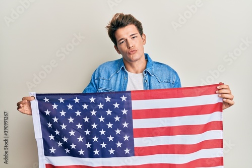 Handsome caucasian man holding united states flag looking at the camera blowing a kiss being lovely and sexy. love expression.