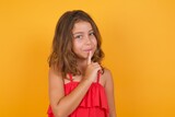 young Caucasian girl standing against yellow background holding hand near face. 