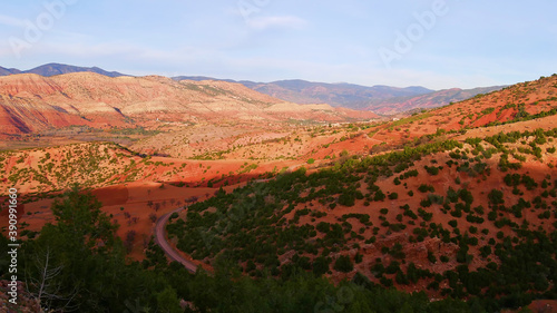 Beautiful panorama view of the red colored foothills of Atlas Mountains near Ouzoud, Morocco, Africa with road and forest in the evening light.