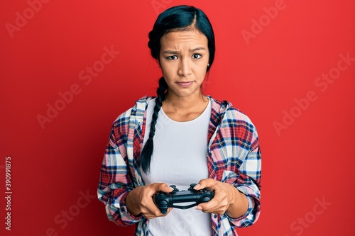 Beautiful hispanic woman playing video game holding controller skeptic and nervous, frowning upset because of problem. negative person.