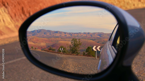 Beautifully red colored foothills of the stunning Atlas Mountains in the evening sun with paved street and road signs near Ouzoud, Morocco viewed in the side mirror of a small car. Focus on center. © Timon