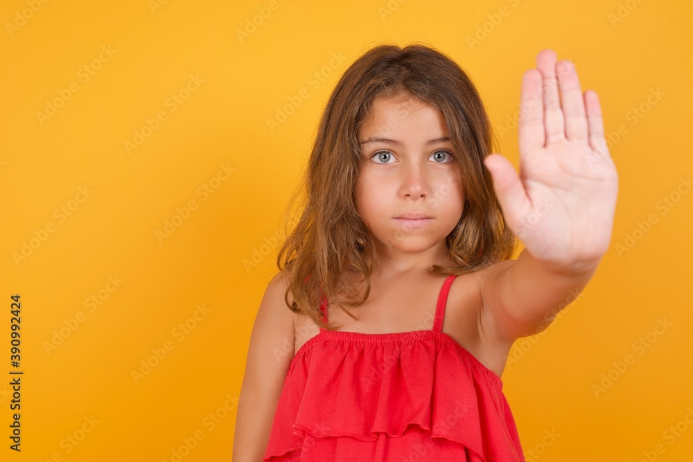 Caucasian young girl standing against yellow background doing stop gesture with palm of the hand. Warning expression with negative and serious gesture on the face.