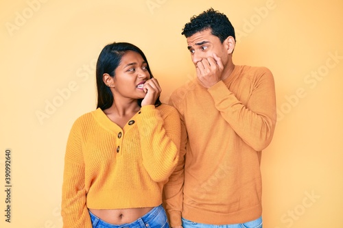 Beautiful latin young couple wearing casual clothes together looking stressed and nervous with hands on mouth biting nails. anxiety problem.