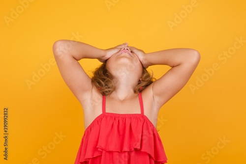 Shocked Caucasian young girl standing against yellow background holding hands on face covering eyes and screaming in despair and frustration while being full of terror, mouth dropped open.