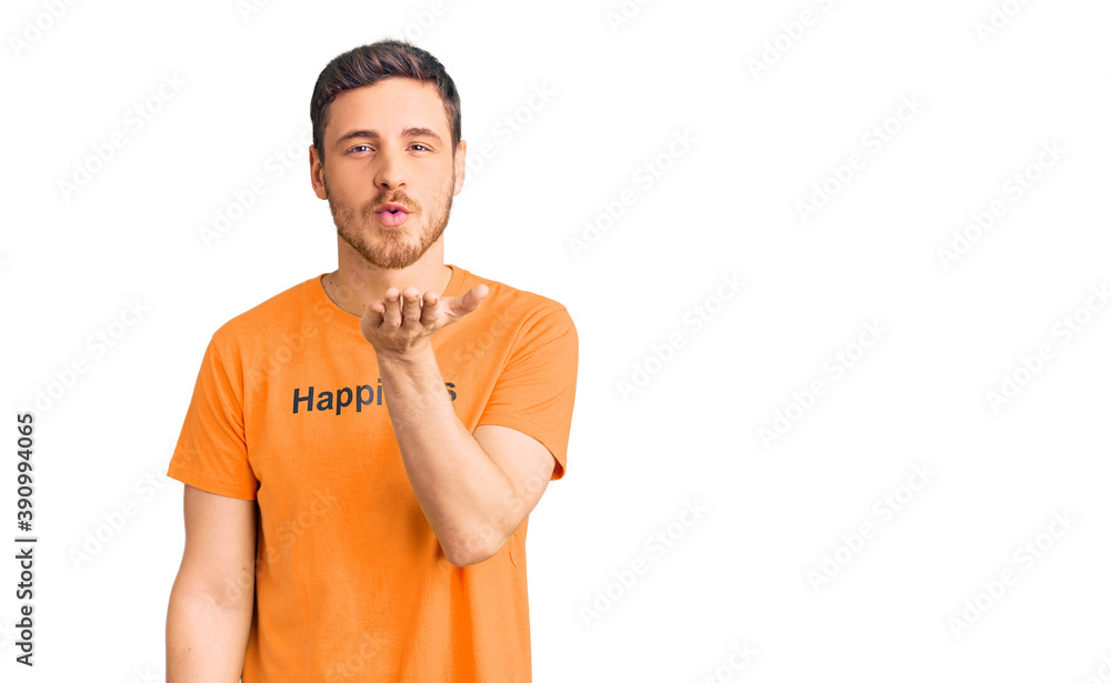 Handsome young man with bear wearing tshirt with happiness word message looking at the camera blowing a kiss with hand on air being lovely and sexy. love expression. Handsome young man with bear wearing tshirt with happiness word message looking at the camera blowing a kiss with hand on air being lovely and sexy. love expression.