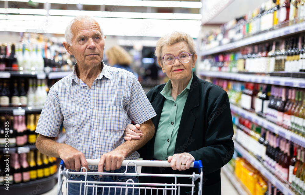 mature couple chooses bottle of wine in alcohol section of supermarket