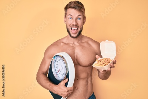 Young caucasian man shirtless holding weighing machine and fried potatoes celebrating crazy and amazed for success with open eyes screaming excited.