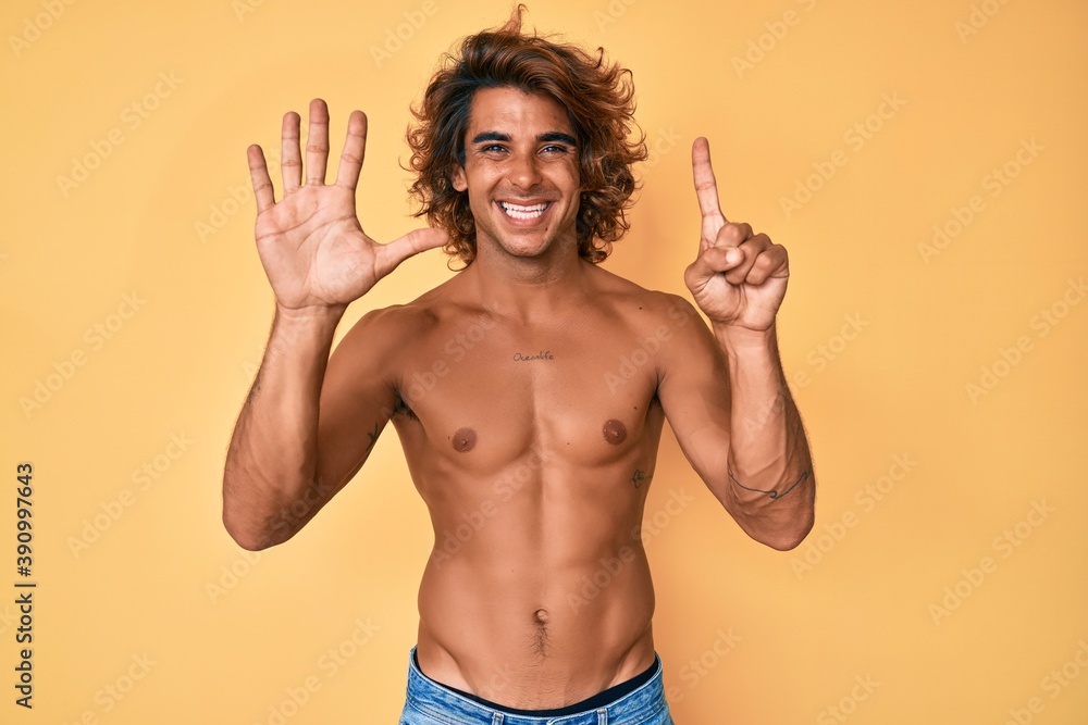 Fototapeta premium Young hispanic man standing shirtless showing and pointing up with fingers number six while smiling confident and happy.