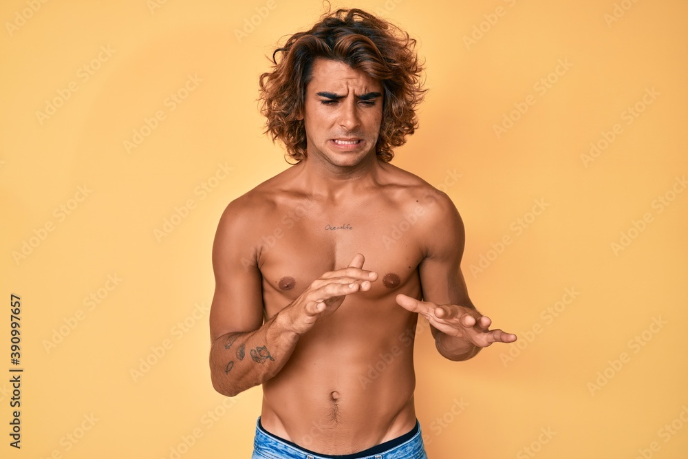 Fototapeta premium Young hispanic man standing shirtless disgusted expression, displeased and fearful doing disgust face because aversion reaction.