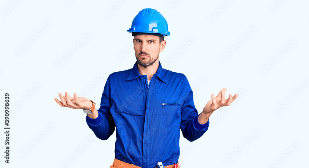 Young handsome man wearing worker uniform and hardhat doing bunny ears gesture with hands palms looking cynical and skeptical. easter rabbit concept.