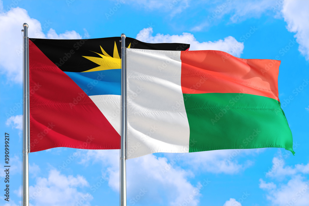 Madagascar and Antigua and Barbuda national flag waving in the windy deep blue sky. Diplomacy and international relations concept. Madagascar and Antigua and Barbuda national flag waving in the windy deep blue sky. Diplomacy and international relations concept.