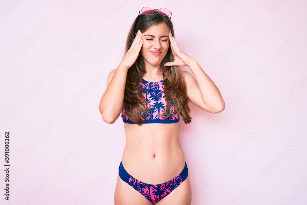 Beautiful young caucasian woman wearing bikini and sunglasses with hand on head for pain in head because stress. suffering migraine. Beautiful young caucasian woman wearing bikini and sunglasses with hand on head for pain in head because stress. suffering migraine.
