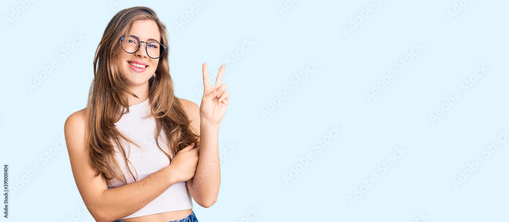Beautiful caucasian young woman wearing casual clothes and glasses smiling with happy face winking at the camera doing victory sign. number two. Beautiful caucasian young woman wearing casual clothes and glasses smiling with happy face winking at the camera doing victory sign. number two.
