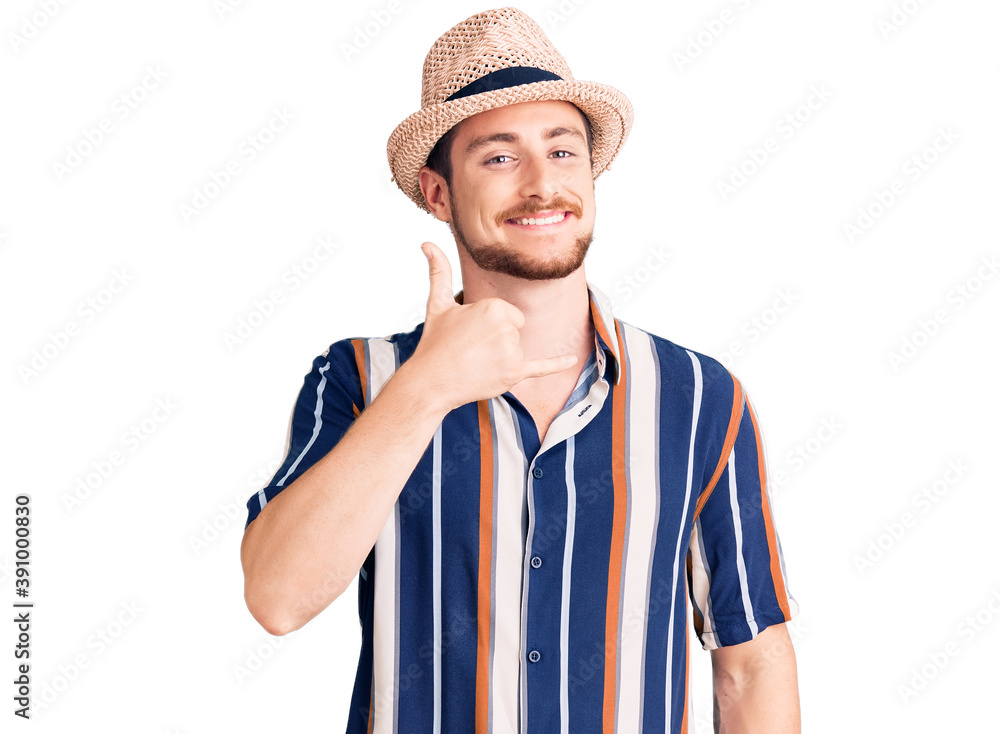 Young handsome caucasian man wearing summer hat smiling doing phone gesture with hand and fingers like talking on the telephone. communicating concepts. Young handsome caucasian man wearing summer hat smiling doing phone gesture with hand and fingers like talking on the telephone. communicating concepts.