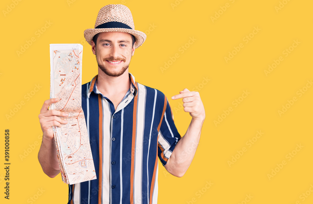 Young handsome caucasian man wearing summer hat holding city map pointing finger to one self smiling happy and proud Young handsome caucasian man wearing summer hat holding city map pointing finger to one self smiling happy and proud