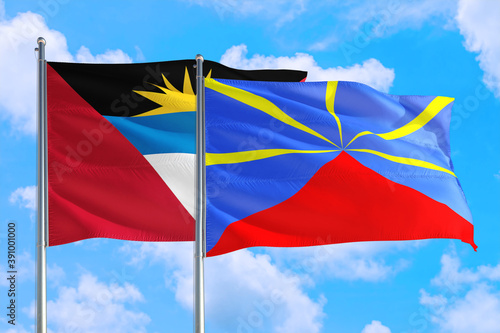 Reunion and Antigua and Barbuda national flag waving in the windy deep blue sky. Diplomacy and international relations concept.