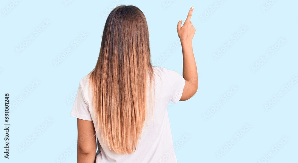 Beautiful caucasian woman wearing casual white tshirt posing backwards pointing ahead with finger hand Beautiful caucasian woman wearing casual white tshirt posing backwards pointing ahead with finger hand