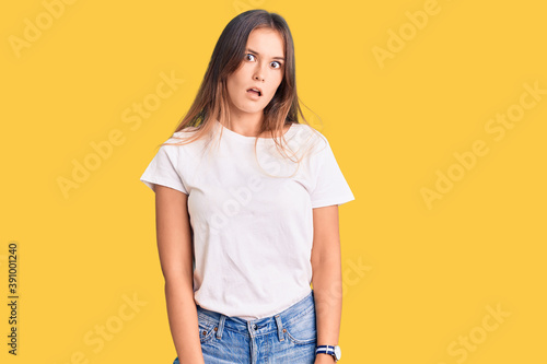 Beautiful caucasian woman wearing casual white tshirt in shock face, looking skeptical and sarcastic, surprised with open mouth
