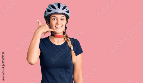 Beautiful caucasian woman wearing bike helmet smiling doing phone gesture with hand and fingers like talking on the telephone. communicating concepts.