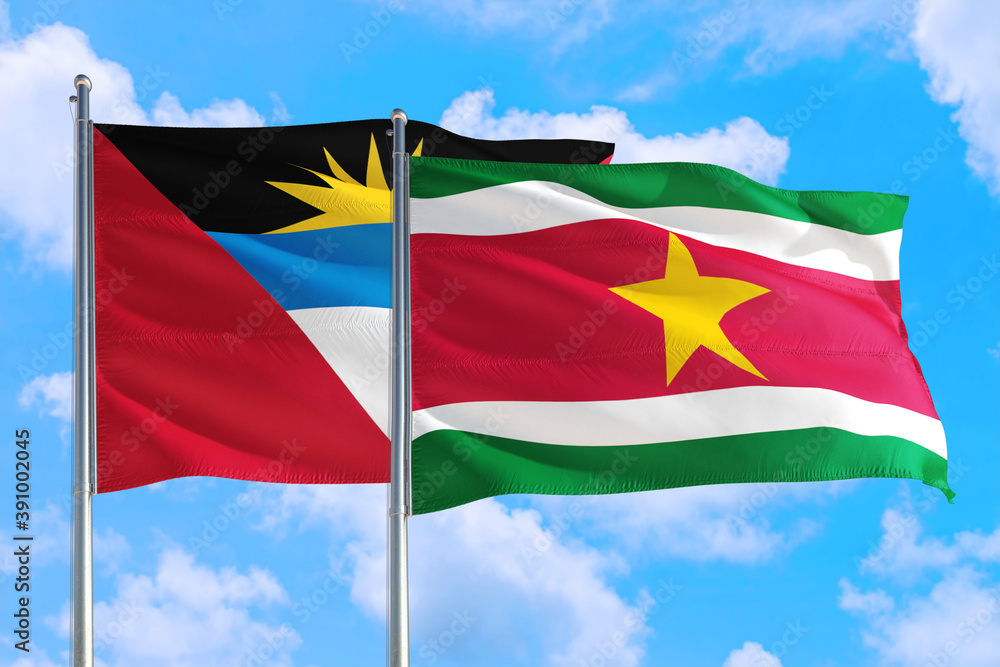 Suriname and Antigua and Barbuda national flag waving in the windy deep blue sky. Diplomacy and international relations concept. Suriname and Antigua and Barbuda national flag waving in the windy deep blue sky. Diplomacy and international relations concept.