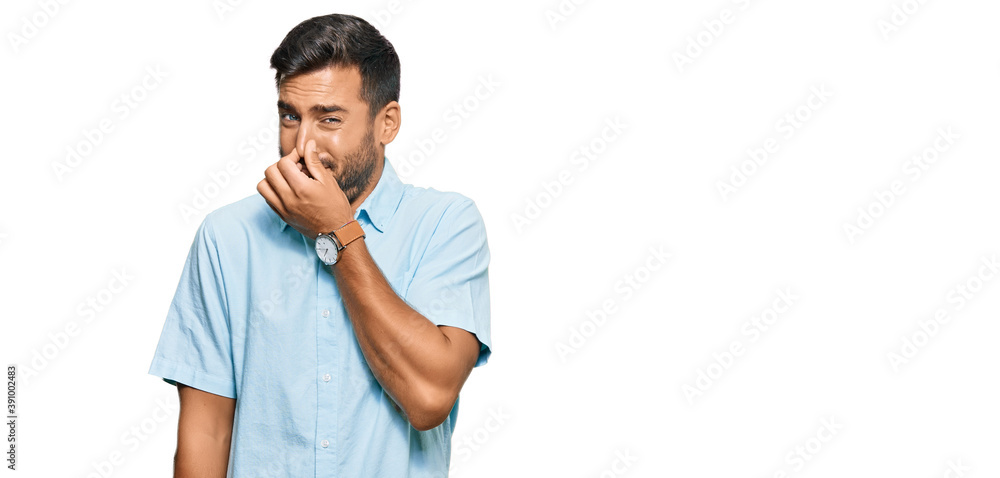 Handsome hispanic man wearing casual clothes smelling something stinky and disgusting, intolerable smell, holding breath with fingers on nose. bad smell Handsome hispanic man wearing casual clothes smelling something stinky and disgusting, intolerable smell, holding breath with fingers on nose. bad smell