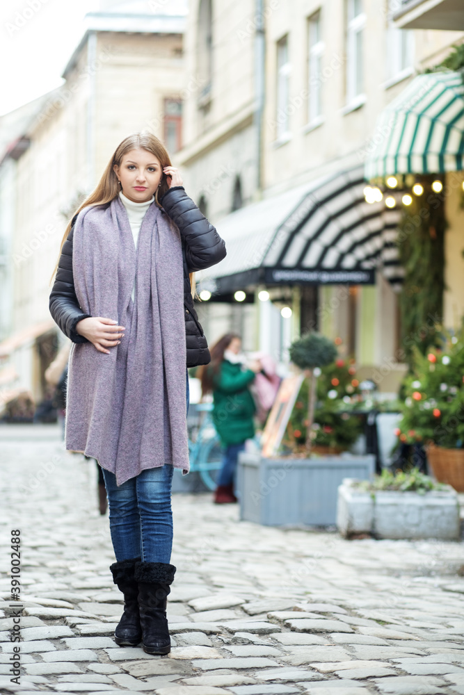A girl in a coat and a long scarf walks around the city, walking along Christmas shops and shop Windows, walking along old streets