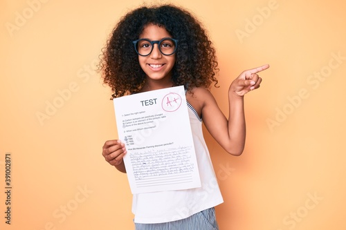 African american child with curly hair wearing glasses showing a passed exam smiling happy pointing with hand and finger to the side