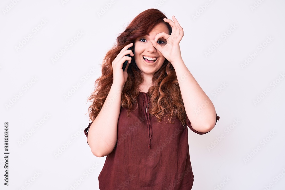 Young beautiful woman having conversation talking on the smartphone smiling happy doing ok sign with hand on eye looking through fingers Young beautiful woman having conversation talking on the smartphone smiling happy doing ok sign with hand on eye looking through fingers