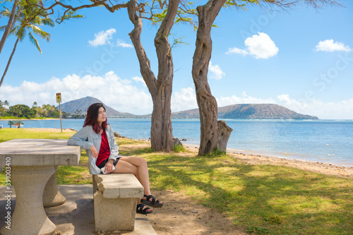 Teen girl relaxing on shaded bench by Hawaiian ocean