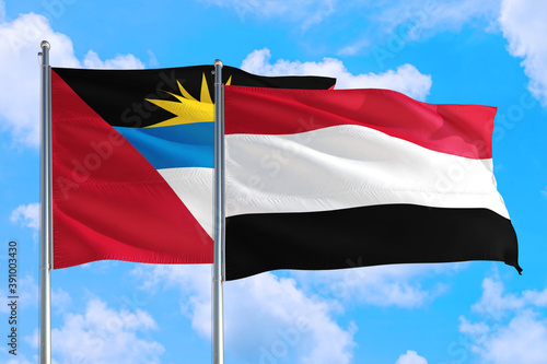 Yemen and Antigua and Barbuda national flag waving in the windy deep blue sky. Diplomacy and international relations concept.