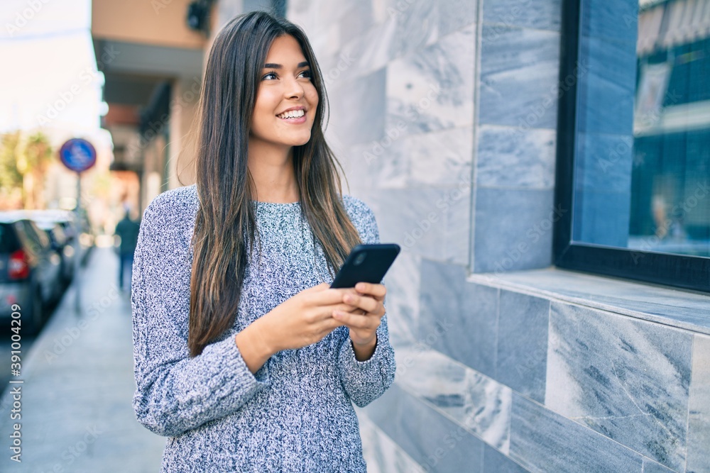 Young beautiful hispanic girl smiling happy using smartphone at the city.