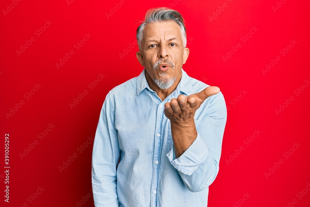 Middle age grey-haired man wearing casual clothes looking at the camera blowing a kiss with hand on air being lovely and sexy. love expression. Middle age grey-haired man wearing casual clothes looking at the camera blowing a kiss with hand on air being lovely and sexy. love expression.