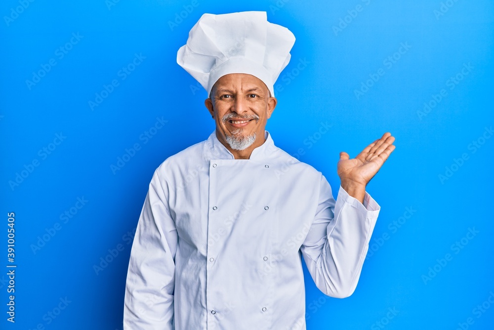 Middle age grey-haired man wearing professional cook uniform and hat smiling cheerful presenting and pointing with palm of hand looking at the camera. Middle age grey-haired man wearing professional cook uniform and hat smiling cheerful presenting and pointing with palm of hand looking at the camera.