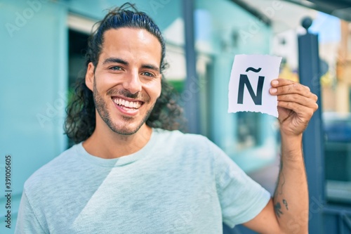 Young hispanic man smiling happy holding paper with ñ letter at city. photo