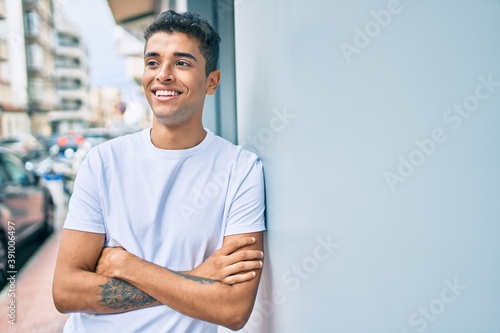 Young latin man smiling happy leaning on the wall at the city.
