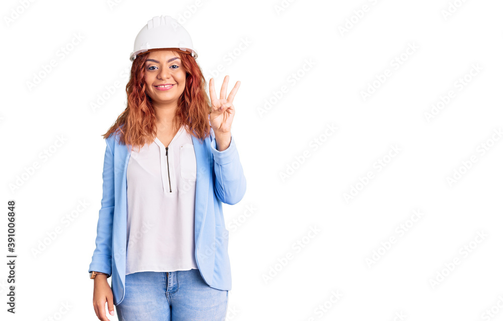 Young latin woman wearing architect hardhat showing and pointing up with fingers number three while smiling confident and happy. Young latin woman wearing architect hardhat showing and pointing up with fingers number three while smiling confident and happy.