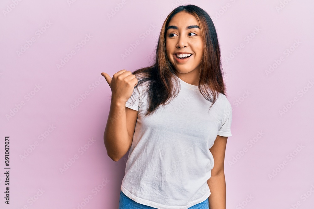 Young latin woman wearing casual white tshirt pointing thumb up to the side smiling happy with open mouth Young latin woman wearing casual white tshirt pointing thumb up to the side smiling happy with open mouth