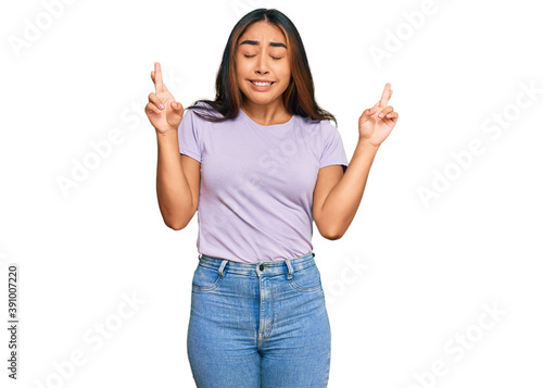 Young latin woman wearing casual clothes gesturing finger crossed smiling with hope and eyes closed. luck and superstitious concept.