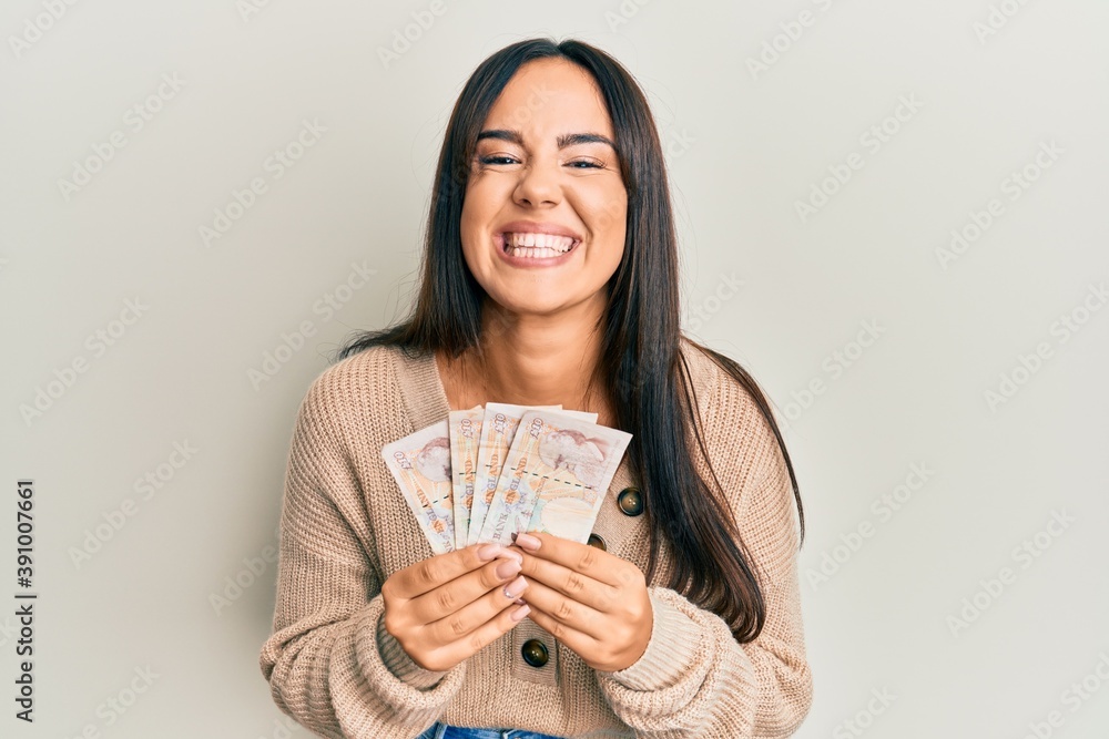 Young beautiful hispanic girl holding 10 united kingdom pounds banknotes smiling and laughing hard out loud because funny crazy joke. Young beautiful hispanic girl holding 10 united kingdom pounds banknotes smiling and laughing hard out loud because funny crazy joke.