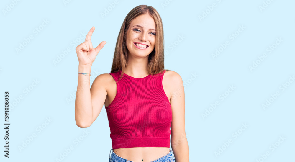 Young beautiful blonde woman wearing elegant summer shirt smiling and confident gesturing with hand doing small size sign with fingers looking and the camera. measure concept. Young beautiful blonde woman wearing elegant summer shirt smiling and confident gesturing with hand doing small size sign with fingers looking and the camera. measure concept.