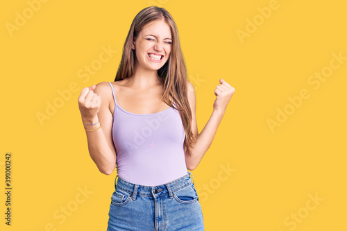 Young beautiful blonde woman wearing casual style with sleeveless shirt very happy and excited doing winner gesture with arms raised, smiling and screaming for success. celebration concept.