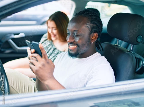 Young interracial couple smiling happy using smartphone at the car.