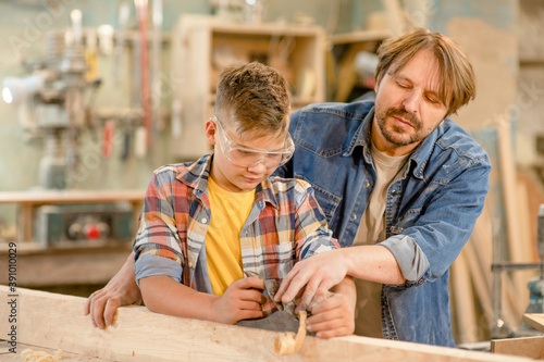 Carpenter teaches young boy to plan wood in a carpentry workshop