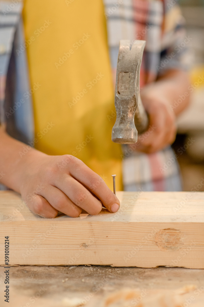 Close up boy hammering a nail in wooden plank