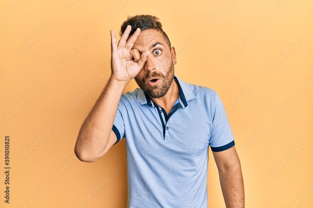Handsome man with beard wearing casual clothes doing ok gesture shocked with surprised face, eye looking through fingers. unbelieving expression. Handsome man with beard wearing casual clothes doing ok gesture shocked with surprised face, eye looking through fingers. unbelieving expression.