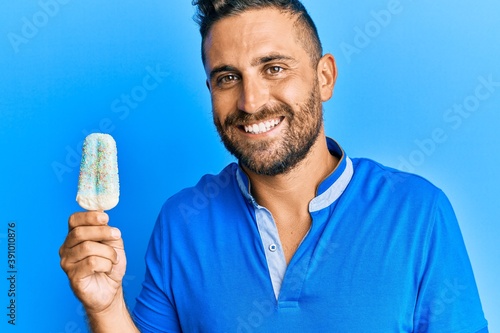 Handsome man with beard holding ice cream looking positive and happy standing and smiling with a confident smile showing teeth